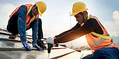 Two people in helmets working on a roof.