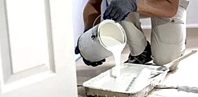 Painter pouring paint from a can into a paint tray.